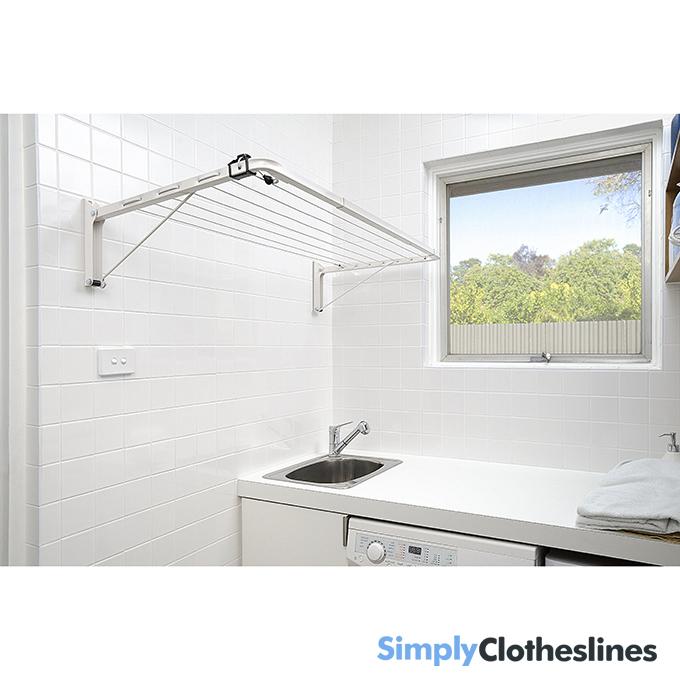 Lifestyle view of the Austral Indoor Outdoor fold down clothesline installed in a compact laundry area with a view through a window.