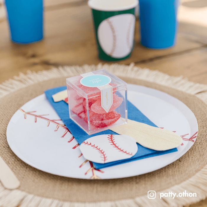 Baseball stitch plate with a blue napkin, paper bat, and a candy cube on a woven charger with blue cups