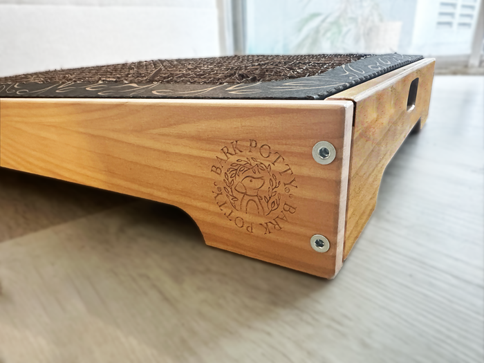 Close-up corner of the wooden Bark Potty tray showing the burned-in Bark Potty logo on the side panel.
