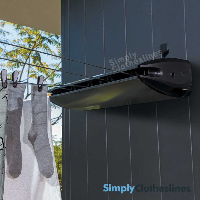 Hills Retractable 5 Line clothesline installed on a dark outdoor wall with garments hanging to dry.