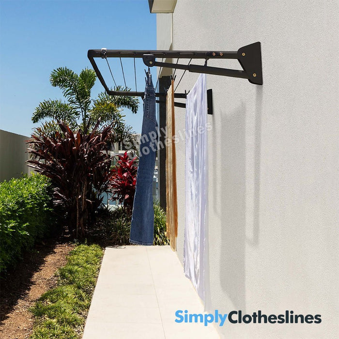 Hills Compact Fold Down clothesline installed on an outdoor wall with garments hanging to dry in a sunny garden setting.