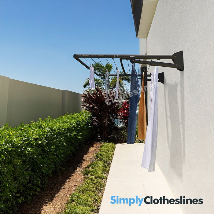 Hills Double Fold Down clothesline installed on an outdoor wall with garments hanging to dry in a sunny garden setting.