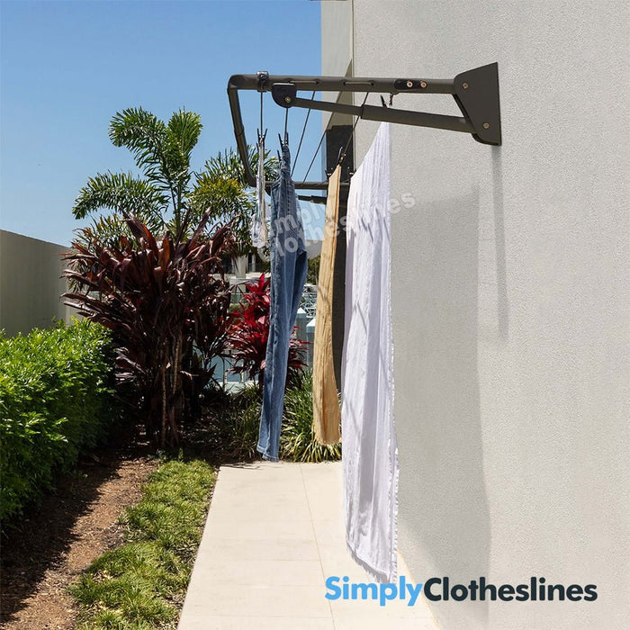Hills Long Fold Down clothesline installed on an outdoor wall with garments hanging to dry in a sunny garden setting.