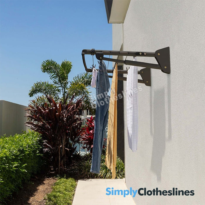 Hills Mini Fold Down clothesline installed on an outdoor wall with garments hanging to dry in a sunny garden setting.