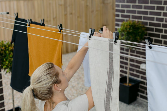 Hills Soft Grip pegs being used by a person to hang a large towel on an outdoor retractable clothesline.