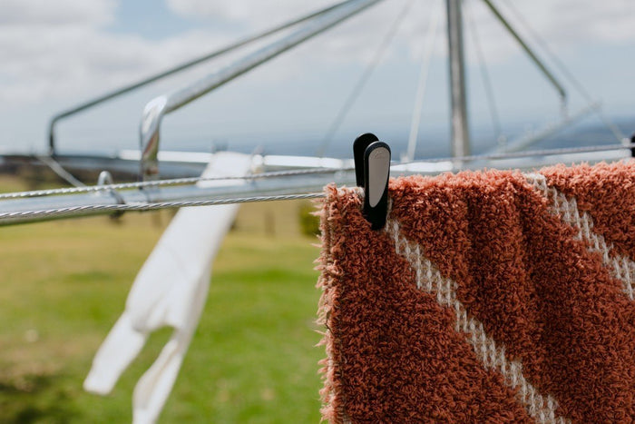 Hills Soft Grip pegs shown in a lifestyle setting, securing a heavy towel and a garment on a hanger to an outdoor rotary clothesline.