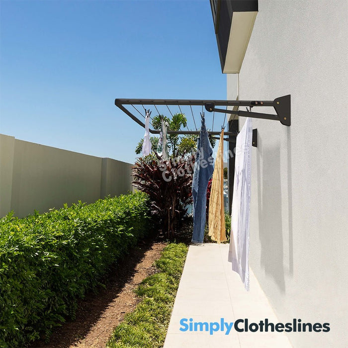 Hills Single Fold Down clothesline installed on an outdoor wall with garments hanging to dry in a sunny garden setting.