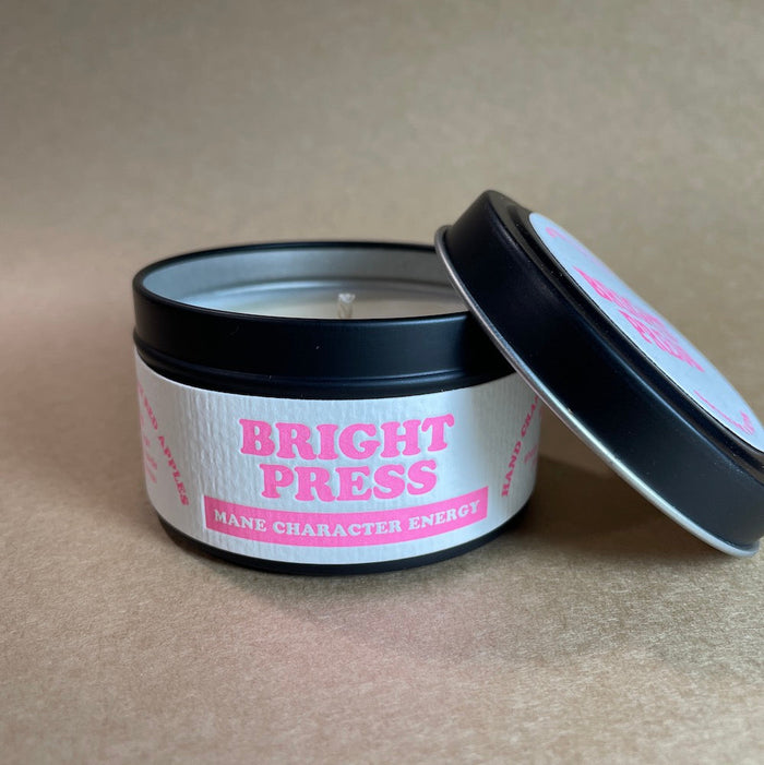 Candle in a black tin with 'Bright Press Mane Character Energy' label on a beige background