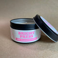 Candle in a black tin with 'Bright Press Mane Character Energy' label on a beige background