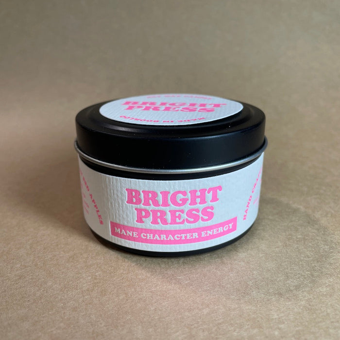 Tin of 'Bright Press Mane Character Energy' soy wax candle on a brown background