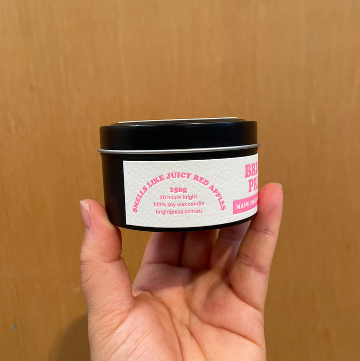Hand holding a candle tin with a label with the side text reading "smells like juicy red apples" against a wooden background