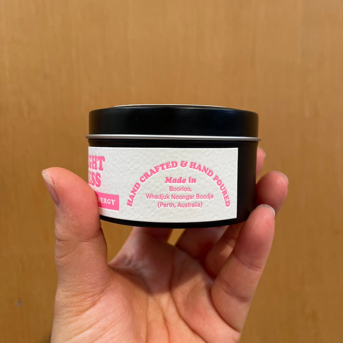 Hand holding a candle tin with a label with the side text reading "hand crafted & hand poured" against a wooden background