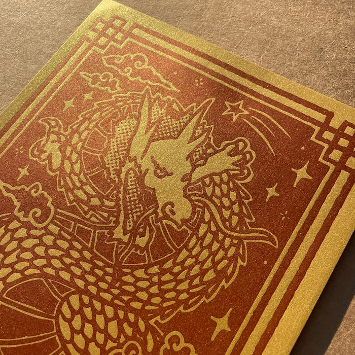 Close-up of the Year of the Dragon print showing off the red ink on the super metallic gold paper on a brown textured surface