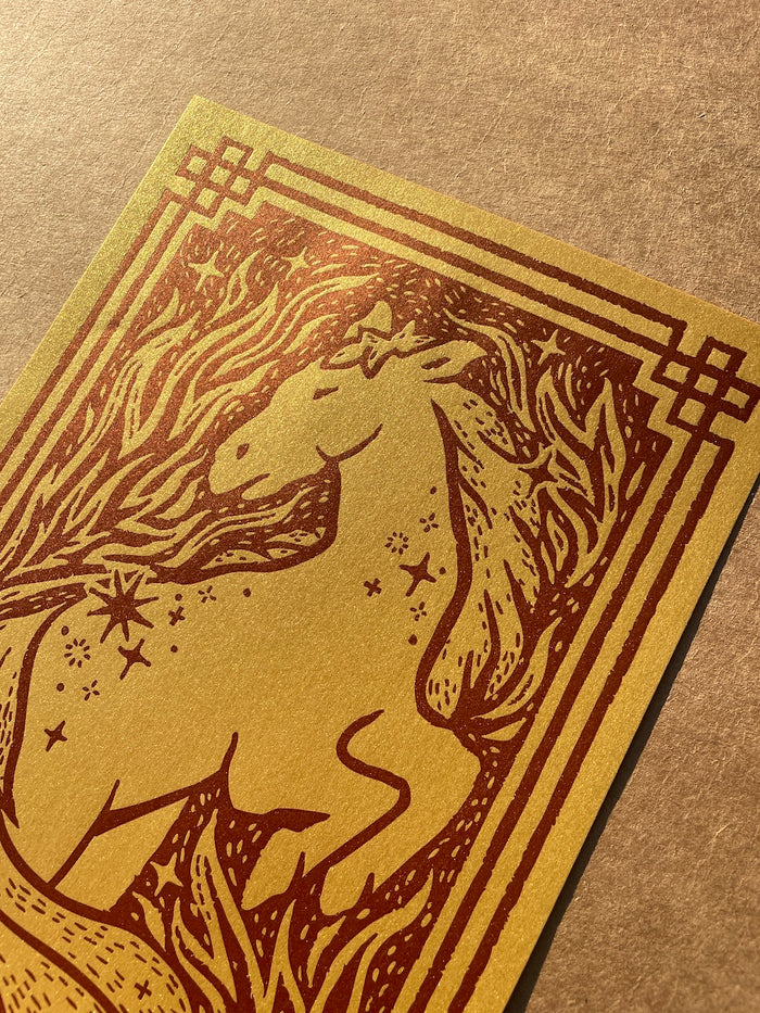 Close up of the horse illustration printed with dark red ink on metallic gold paper on a brown background