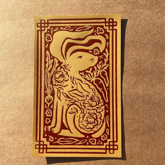 Year of the Rabbit print featuring a rabbit looking to the right with decorative cabbage on its body and carrots and foliage and a decorative border surrounding the rabbit on a brown textured background