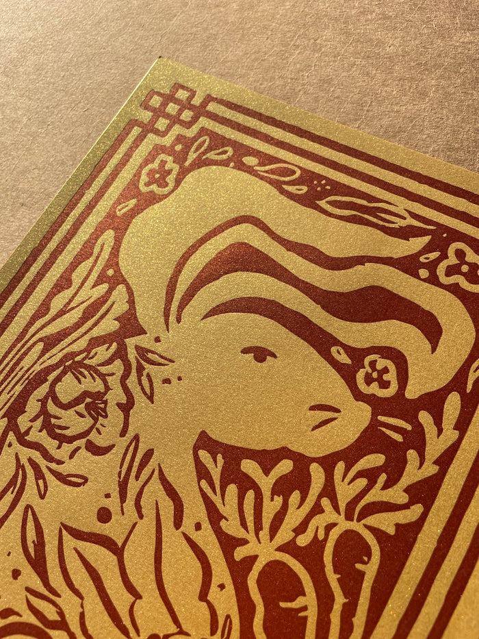 Close up of the print featuring the rabbit design printed in dark red on super metallic gold stock